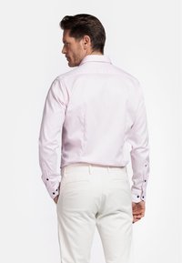 Lichtroze langemouwen shirt met een soepele textuur, voorzien van zwarte knoopaccenten bij de manchetten, gecombineerd met witte broeken.