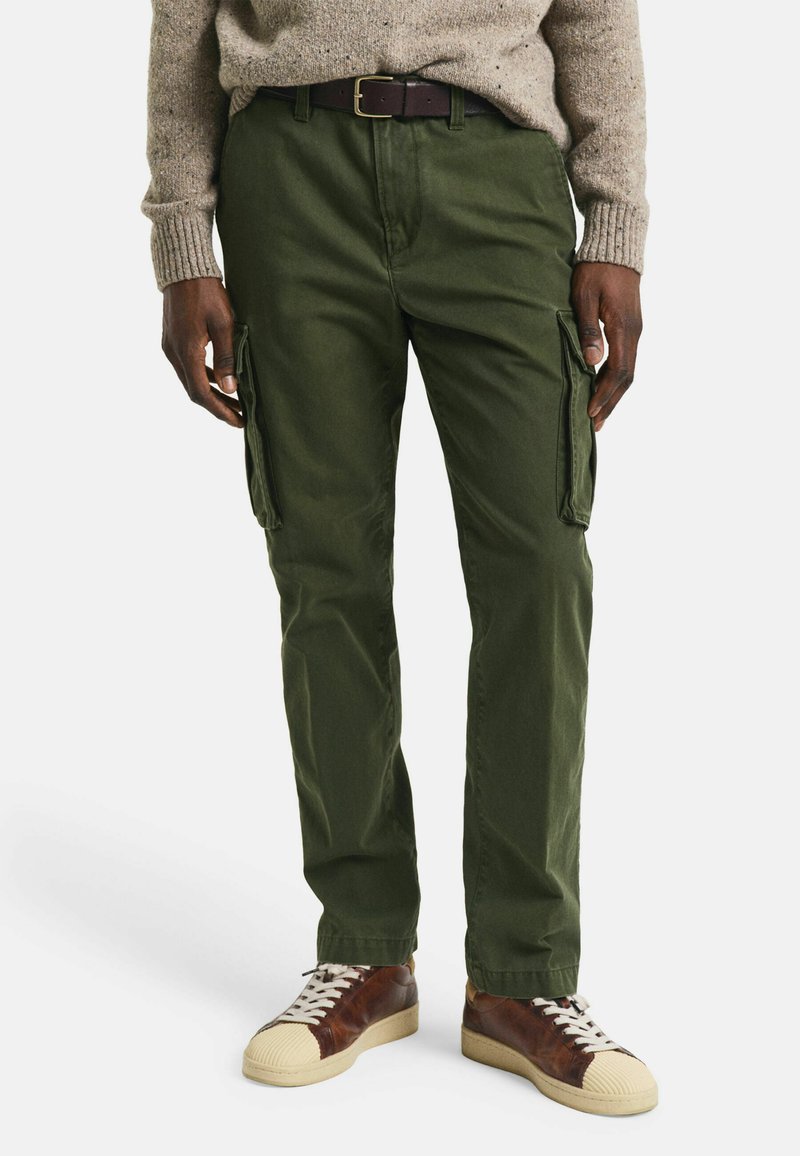 Cargo-Hosen in olivgrün, aus strapazierfähigem Stoff, mit seitlichen Taschen und geradem Bein. Kombiniert mit braunen und cremigen Sneakers.