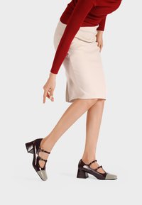 Los zapatos Mary Jane de charol presentan un empeine burdeos con una puntera gris y dos tiras decorativas. Diseño de tacón cuadrado.