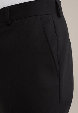 Pantalons noirs ajustés avec une texture en chevrons, poches latérales et passants de ceinture. Le tissu semble lisse et structuré.