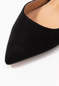 Chaussure plate à bout pointu en daim noir avec une texture lisse, une couture subtile le long de l'ouverture et une doublure intérieure beige.