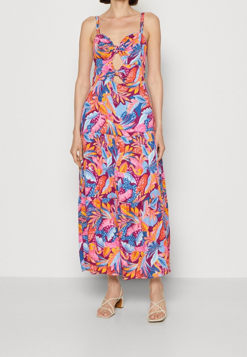 Robe maxi à imprimé floral avec des teintes vibrantes de rose, bleu et orange. Elle possède des bretelles fines et un détail torsadé au niveau de la poitrine.