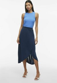 Niebieski, prążkowany top na ramiączkach w zestawieniu z granatową spódnicą w stylu owijanym. Spódnica ma wysoki rozcięcie i jest wykonana z gładkiej, elastycznej tkaniny.