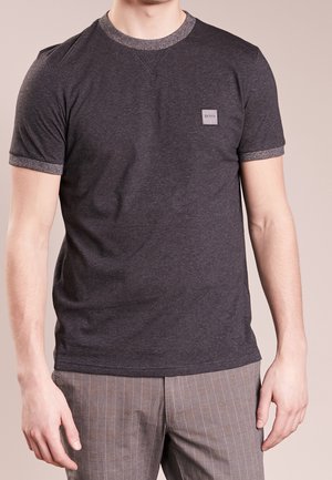 Mann trägt ein dunkelgraues kurzärmeliges T-Shirt mit kleinem "BOSS"-Logo auf der linken Brust und graue Nadelstreifenhose.