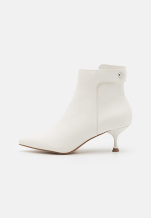 Weißer Knöchelstiefel mit spitzer Zehe, aus glattem Material gefertigt, mit einem schlanken Absatz und einem Riemen mit Druckknopfakzent.