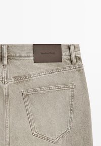 Achteraanzicht van lichtbeige spijkerbroek met één achterzak en een bruin leren merkembleem met de tekst "Massimo Dutti".