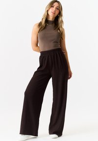 Brown sleeveless top paired with black textured wide-leg pants featuring an elastic waist. White sneakers accent the outfit.