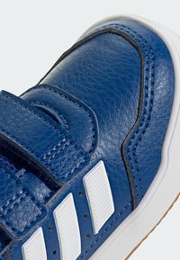 Niebieski but ze sztucznej skóry z białymi paskami na rzep, o fakturowanej powierzchni i kontrastującym czarnym przeszyciem. Zawiera trzy białe paski akcentujące.