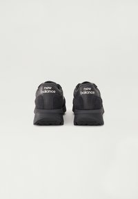 Chaussures de sport noires avec un dessus texturé, portant le logo "New Balance" au talon et une semelle en caoutchouc robuste pour le soutien.