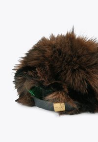 Brązowy futrzany kapelusz o puszystej fakturze, z czarną tkaniną wzdłuż i zielonym wykończeniem w środku. Złote okucia z nazwą marki.