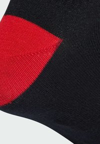 Černá ponožka s texturovaným červeným detailem na patě, vyrobená z elastické látky pro pohodlí a dobré přizpůsobení.