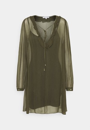 Blouse verte olive transparente avec un col en V, bordure à volants et manches longues. Dotée d'une fermeture à nouer et d'accents métalliques sur les poignets.