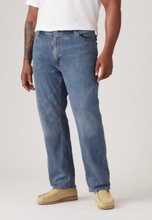 Blaue Denim-Jeans mit lockerer Passform, die über ein klassisches Fünf-Taschen-Design und gestickte Details verfügen. Kombiniert mit hellbraunen Mokassins.
