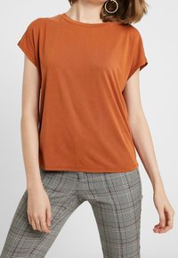 Brown short-sleeve t-shirt with a round neck, smooth texture, worn with gray plaid pants. Features a loose fit and hemmed edges.