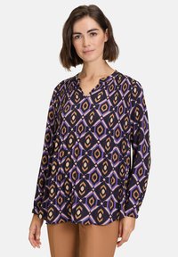 Long-sleeve blouse in black with diamond pattern in brown, purple, and beige. Features a V-neck and gathering details at the shoulders.