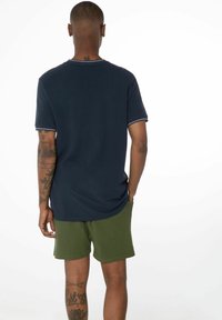 T-shirt à manches courtes navy avec des Bordures blanches, associé à un short vert olive. Ses caractéristiques incluent une coupe décontractée et une texture textile.