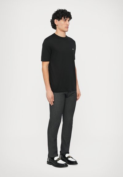 Juoda trumpomis rankovėmis marškinėliai, pilkos plonos kelnės ir juodi batai su baltais akcentais. Paprastas dizainas, minkšta medžiaga ir minimalūs dekoratyviniai elementai.