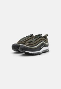Sníhací Nike Air Max 97 v olivově zelené, černé a bílé barvě. Disponují vlnitým, vrstveným designem s materiály z mešové tkaniny a gumy, viditelným vzduchovým polstrováním.