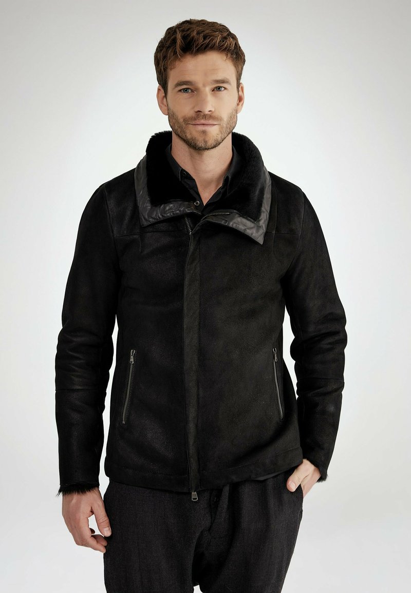 Schwarze Jacke aus einem wildlederartigen Material, mit einem breiten Kragen, zwei Reißverschlusstaschen und einer taillierten Passform mit strukturierten Akzenten.