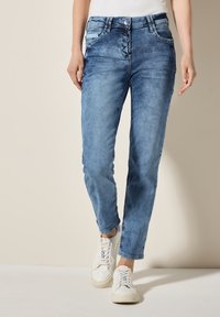 Jeans in denim azzurro chiaro con una vestibilità slim, dettagli di whiskering e cinque tasche, abbinati a sneakers bianche.