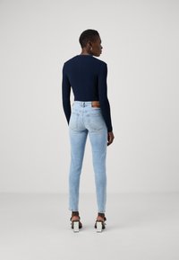 Mörkblå långärmad ribbad topp i kombination med ljusblå skinny jeans. Skorna har en vit kvadratisk klack och svarta remmar. Prislappen synlig på jeansen.