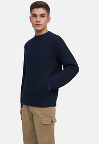 Navy blue knitted sweater with textured fabric, round neckline, and ribbed cuffs and hem. Paired with khaki cargo pants featuring pockets.