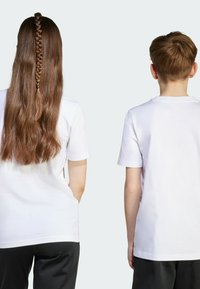 White cotton t-shirts worn by a teenager and a child, visible from the back. The teenager has long, wavy hair with a braided section.