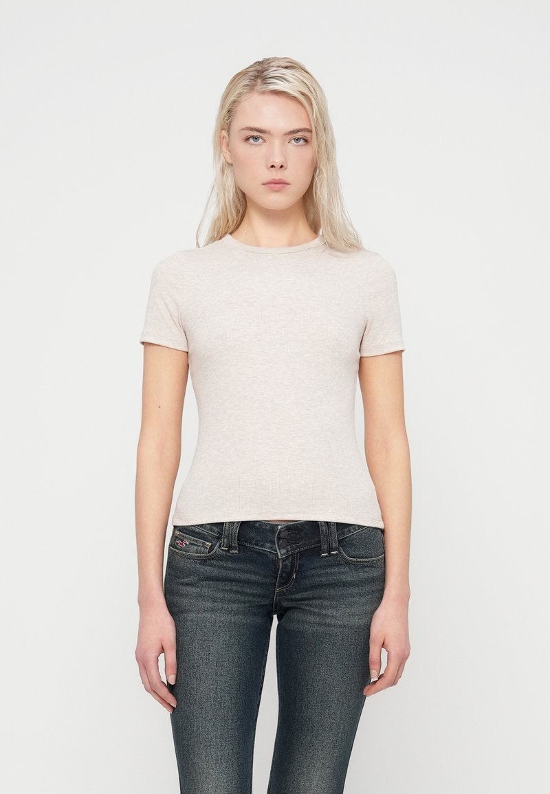 Φανελάκι σε ανοιχτό γκρι χρώμα, εφαρμοστό, με κοντά μανίκια και στρογγυλή λαιμόκοψη, σε συνδυασμό με τζιν σε σκούρο πλύσιμο. Ομαλή υφή, μινιμαλιστικός σχεδιασμός, χωρίς διακοσμητικά στοιχεία.