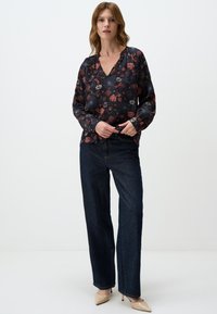 Camicia scura con motivo floreale, scollo a V e maniche lunghe, abbinata a jeans ampi blu scuro e décolleté beige a punta.