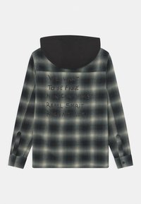 Camicetta a scacchi con tonalità nero e grigio, dotata di cappuccio e testo stampato sul retro. Polsini con bottoni e vestibilità rilassata. Texture del tessuto visibile.