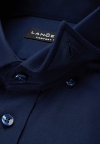 Granatowa koszula z kołnierzykiem o fakturowanej tkaninie, z zapięciem na guziki z przodu i metką z napisem "LANCER" w kolorze czarnym. Niebieskie guziki z motywem kwiatowym.