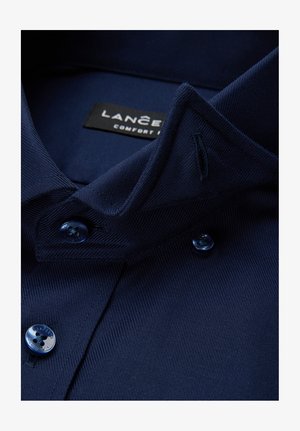 Granatowa koszula z kołnierzykiem o fakturowanej tkaninie, z zapięciem na guziki z przodu i metką z napisem "LANCER" w kolorze czarnym. Niebieskie guziki z motywem kwiatowym.