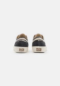 Black and cream canvas slip-on shoes with a textured finish, contrasting stitching, and a signature logo tag on the heel.