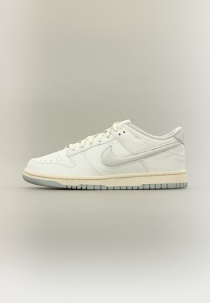 Baskets basses blanches Nike avec une semelle intermédiaire crème, une semelle extérieure grise, un design à lacets et le logo emblématique Nike swoosh sur le côté.