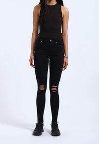 Svarta högmidjade skinny jeans med slitna knän, kombinerat med en åtsittande svart tanktop och svarta sportskor.