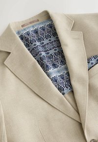 Bézs texturált blézer részletes kék-fehér virágmintás béléssel és hozzá illő zsebkendővel.