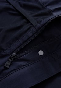 Interior de chaqueta navy con tejido texturizado, con un detalle de cremallera y botón a presión. Material suave con un acabado mate.