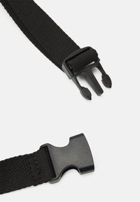 Cinturino intrecciato nero con una fibbia in plastica nera a rilascio laterale non allacciata su uno sfondo bianco.