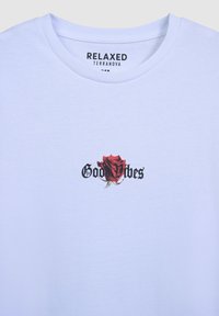 Biała bawełniana koszulka z grafiką czerwonej róży i czarnym tekstem "Good Vibes". Luźny krój przy szyi, miękka tekstura, casualowy design.