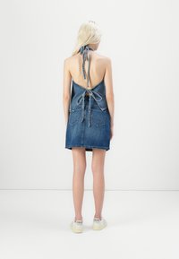 Denim halter obleka z odprtim hrbtom, zveznim detajlom, dvema žepoma na hrbtu in kratkim krilom. Končan rob z svetlo modrim pranjem.