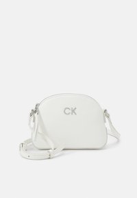 Bílá kožená crossbody taška zaobleného tvaru, se stříbrným zipem a logem. Obsahuje nastavitelné ramenní popruhy a hladký povrch.