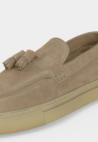 Loafer από ανοιχτό καφέ σουέτ με στρογγυλεμένο μπροστινό μέρος, διπλά φουντάκια στην καμάρα και μπεζ λαστιχένια σόλα.