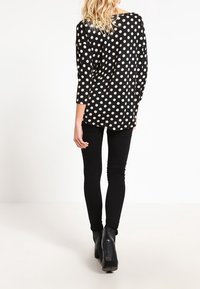 Schwarz gepunktete Bluse mit Dreiviertelärmeln, lockere Passform und rundem Ausschnitt, kombiniert mit schwarzen Skinny-Jeans und Ankle Boots.
