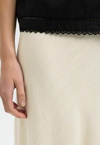 Top court noir avec dentelle au niveau de l'ourlet, superposé sur une jupe texturée de couleur crème avec un motif diagonal. Main reposant sur la jupe.