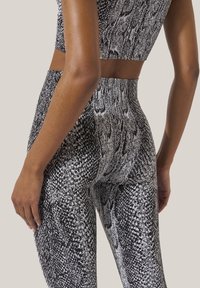 Leggings en imprimé serpent noir et blanc, fabriqués en tissu extensible, avec une taille haute et une texture lisse.