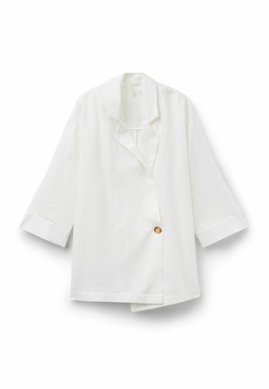 Blazer blanc à manches longues avec de larges revers et un seul bouton visible marron clair sur le devant, présenté à plat sur un fond blanc.