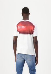 Camiseta blanca de algodón con un diseño de spray rojo degradado en la parte posterior con un logotipo. Mangas cortas y estilo de cuello redondo.