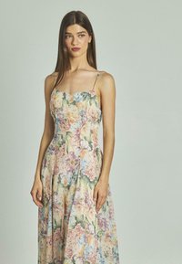 Robe maxi fleurie avec des bretelles spaghetti, présentant des nuances pastel de rose, jaune et vert, fabriquée en tissu léger avec un design fluide.
