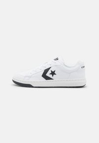 Adidași albi cu logo-ul unei stele negre, din material de piele netedă, cu sistem de șireturi, talpă din cauciuc și accente negre contrastante pe laterale.