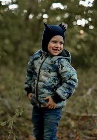 Pūkains, rakstains jaka zilā un zaļā toņos ar tumšiem aprocēm, kopā ar zilām džinsām un tumši zilas cepures ausu formas akcentiem.